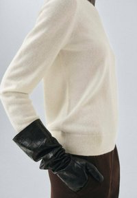 Un pull ivoire avec une texture douce, associé à des gants en cuir noir avec un motif crocodile et un détail froncé au poignet.