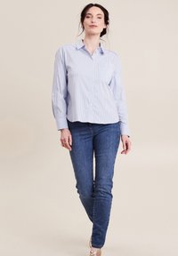 Camicia a righe blu e bianche, con bottoni, maniche lunghe, dotata di taschino sul petto. Abbinata a jeans fitted blu scuro e sandali.