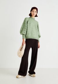 Light green knit sweater with a high neckline and puffed sleeves, paired with brown ribbed wide-leg pants and beige sneakers, holding a cream bag.
