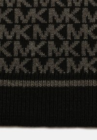 Strikket stof med et gentagende 'MK'-mønster i sort og grå, med en ribbet kant og blød tekstur. Grå accenter skaber kontrast.