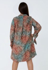 Multikleurige jurk van lichtgewicht stof met een herhalend rond patroon in rood, blauw en beige, met lange mouwen en een losse pasvorm.