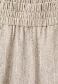 Tissu beige clair avec une finition texturée, présentant des rayures verticales et une taille élastique pour un ajustement réglable.