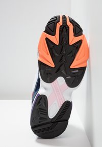 Semelle en caoutchouc noire avec des accents orange et rose. Le motif de semelle présente des crampons triangulaires. Logo Adidas au bas.