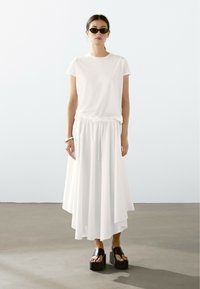Witte t-shirt gecombineerd met een luchtige witte rok met een elastische tailleband. Zwarte chunky platform sandalen zorgen voor contrast. Minimalistisch ontwerp.