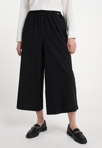 Zwarte wijde broek met een elastische tailleband, gemaakt van lichtgewicht stof. In combinatie met zwarte leren instappers. Glad textuur.