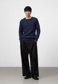 Marineblauer Strickpullover mit strukturiertem Muster, Rundhalsausschnitt und Rippbündchen, kombiniert mit schwarzen weit geschnittenen Hosen und schwarzen Schuhen.