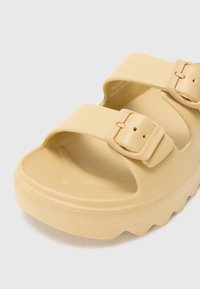 Yellow polymer sandals with a flat sole, featuring two adjustable buckles and a smooth texture, designed for comfort and easy wear.