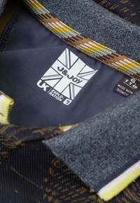 Kraagshirt van marineblauwe stof met meerkleurige patroonaccenten; heeft een stoffen label met merknaam, onderhoudsinstructies en maat.