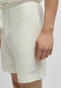 Valkoiset, tekstuuriset shortsit, joissa on ruutukuvio, jossa on nauhavyötär�ö ja pieni brodeerattu "HUGO" -logo helma. 