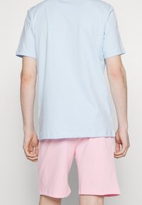 T-shirt en coton bleu clair avec des manches courtes et une coupe décontractée, associé à un short en coton rose, affichant un design simple et une texture douce.