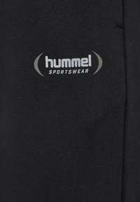 Schwarze Sportbekleidung mit glatter Textur verfügt über ein auffälliges graues "hummel"-Logo und Akzente, die für aktive Nutzung gestaltet sind.