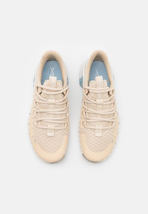 Paire de chaussures de course Nike beiges avec semelles intérieures bleu clair et semelles blanches, vues de dessus sur un fond blanc.