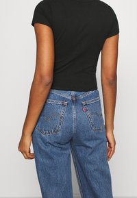 Černá košile s krátkým rukávem spojená s modrými džíny. Džíny mají výrazné zadní kapsy se švy a červenou nášivku.