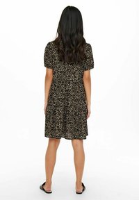 Robe imprimée léopard noire et fauve avec un design à volants, manches courtes bouffantes et coupe ample. Portée avec des sandales plates noires.