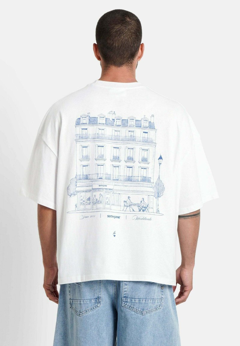 Witte katoenen t-shirt met een blauwe lijntekening van een Parijse gebouw met buitenzitplaatsen, korte mouwen en een ontspannen pasvorm.