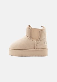 Bottines beiges en daim avec des panneaux latéraux élastiques, un bout rond et une semelle plateforme légère beige montée. Design simple, accents minimalistes.