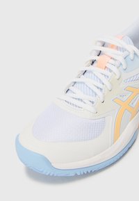 Witte sportschoen met een bovenwerk van mesh, lichtblauwe accenten, oranje highlights en een gestructureerde zool voor grip.