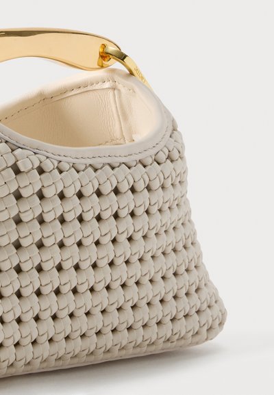 Κοντινό πλάνο μιας μπεζ πλεκτής δερμάτινης τσάντας με καμπυλωτή λαβή από χρυσό μέταλλο και λεπτομερή ραφή κατά μήκος της πάνω άκρης.