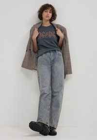 T-shirt di band grafica in grigio scuro, blazer a quadri chiari, jeans larghi in blu scolorito e stivali neri chunky.