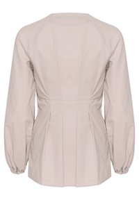 Blouse beige à manches longues pour femme avec poignets froncés, taille ajustée et détail plissé dans le dos.