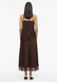 Brūna satīna maksi kleita ar plānām lencītēm un smalkām mežģīnēm apakšmalā. Gluda auduma ar plūstošu dizainu.