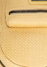 Borsa a tracolla beige intrecciata con superficie texturizzata, dotata di chiusura con zip e un accento in pelle liscia. Forma compatta e rotonda.