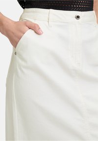 Jupe en denim blanc avec une poche latérale, fermeture à bouton et détails de couture visibles. Texture lisse avec un design ajusté.