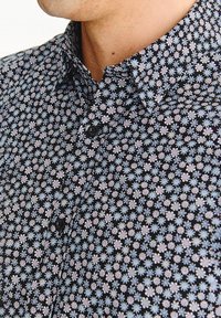 Czarna koszula z guzikami ozdobiona kwiecistym wzorem w jasnoniebieskie i różowe kwiaty, wykonana z materiału o teksturowanym wyglądzie.