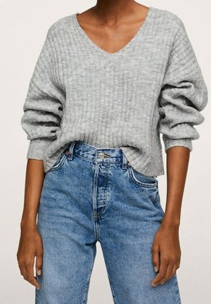 Personne portant un pull en maille côtelée gris clair à col en V avec les manches retroussées, rentrée dans un jean bleu taille haute.