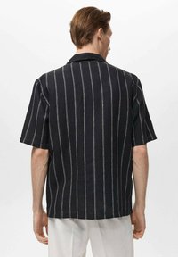Korte mouwen, zwart overhemd met kraag met witte verticale strepen, gemaakt van textuurstof, heeft een losse snit en een rechte zoom.
