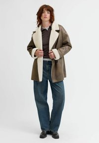 Ruda avių kailiu išklota odinė striukė su plačiu apykakle, ilgomis rankovėmis ir laisvo kirpimo mėlynomis džinsomis. Juodi kulkšnies ilgio batai užbaigia aprangą.