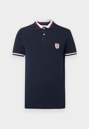 Polo bleu marine à manches courtes avec un col orné de bandes blanches, rouges et bleu marine, des rayures blanches sur les manches et une petite écusson logo sur la poitrine.