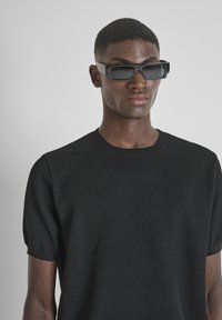 T-shirt nera a coste con maniche corte, dotata di scollatura a girocollo. Abbinata a occhiali da sole neri angolari con lenti scevre.