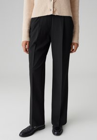 Pantalons noirs ajustés avec une coupe droite, dotés de poches latérales, de détails de plis et d'une finition lisse. Portés avec des mocassins noirs.