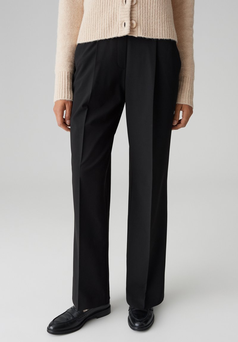 Pantalons noirs ajustés avec une coupe droite, dotés de poches latérales, de détails de plis et d'une finition lisse. Portés avec des mocassins noirs.