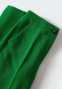 Pantalons verts ajustés avec une texture lisse, dotés d'une fermeture à un bouton et de plis avant. La taille est structurée et large.