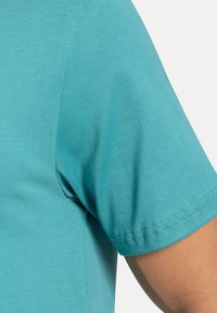 Camicia a maniche corte in tessuto turchese, caratterizzata da una superficie liscia e cuciture pulite all'orlo delle maniche, con una forma aderente.