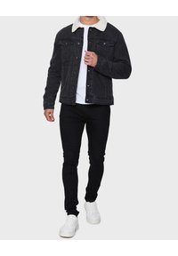 Zwarte spijkerjack met een witte nep-shearling kraag, met knoopsluiting, borstzakken en een versleten textuur; gecombineerd met zwarte skinny jeans en witte sneakers.