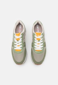 Grüne und graue Sneakers mit einer glatten Textur, weißen Schnürsenkeln, gelben Akzenten und einem gepolsterten Schaftrand. Branding auf der Zunge sichtbar.