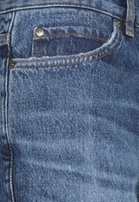 Farkut vaaleansinisellä kuluneella viimeistelyllä. Ominaisuuksina pieni etutasku, kupariset niitit ja ristikkäin oranssia tikkausta saumoissa.