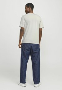 Hellgrau kurzärmliges T-Shirt, lockere Passform, kombiniert mit dunkelblauen, weit geschnittenen Jeans. Sneakers vervollständigen das lässige Outfit, von hinten gezeigt.