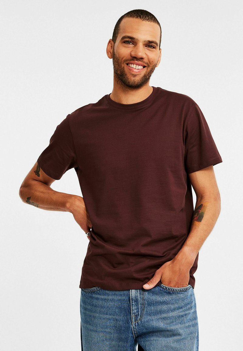 Bordeaux gekleurde t-shirt met korte mouwen, gemaakt van een zachte, gladde stof en met een ronde hals. Gecombineerd met een blauwe spijkerbroek in een casual fit.