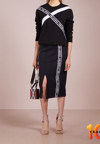 Felpa nera con striscia diagonale bianca e logo; gonna a tubino abbinata con spacco laterale e striscia con logo. Accessori: borsa piccola a fantasia.