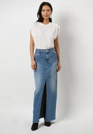 Denim maxi-jurk met een voorpand-split, middelblauwe wassing en rafelige zoom. Gepaarde met een wit shirt en zwarte enkellaarsjes.