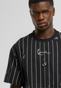 Black short-sleeve T-shirt featuring white vertical stripes and subtle graphic designs, with a round neck and soft cotton texture.