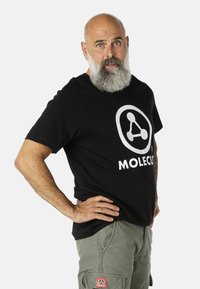 Čierne bavlnené tričko s veľkým bielym logom "Molecu". Krátke rukávy a voľný strih, kombinované s olivovozelenými cargo nohavicami.