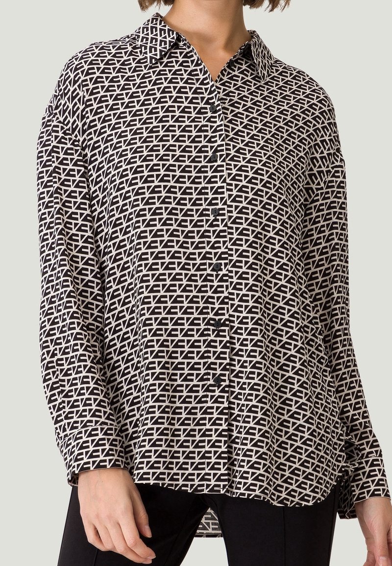 Sort og hvid mønstrede langærmede skjorte med krave, der har et geometrisk design, frontknapper og en let buet kant.