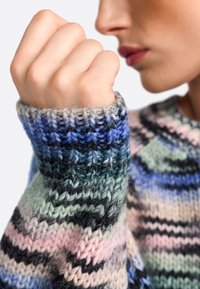 Strickpullover mit einem mehrfarbigen Muster, das grüne, blaue, rosa und schwarze Streifen zeigt. Nahaufnahme der strukturierten Bündchen.