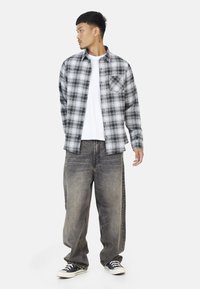Grijze en zwarte geblokte flanellen overhemd over een wit T-shirt, gecombineerd met losse, vervaagde grijze jeans en zwarte sneakers.