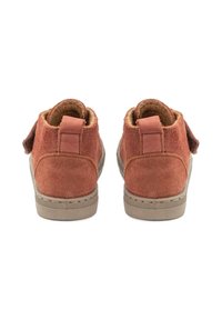 Zapatos de ante marrón hasta el tobillo con una parte superior suave y texturizada, que cuentan con una suela de goma gris y un tacón plano. Incluyen una pestaña en la parte trasera para facilitar el calzado.